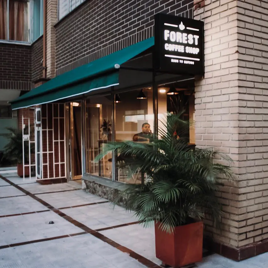 Fachada de Forest Coffee Shop con su aviso, toldo verde y plantas