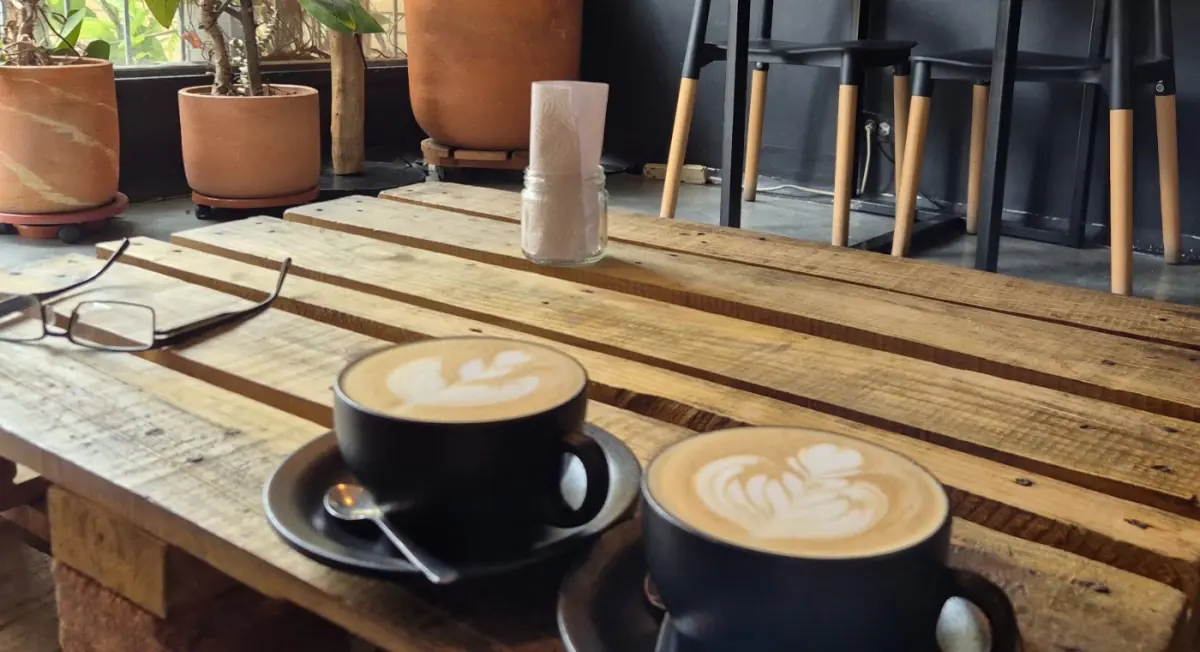 Dos lattes con arte en espuma sobre una mesa de madera rodeada de plantas